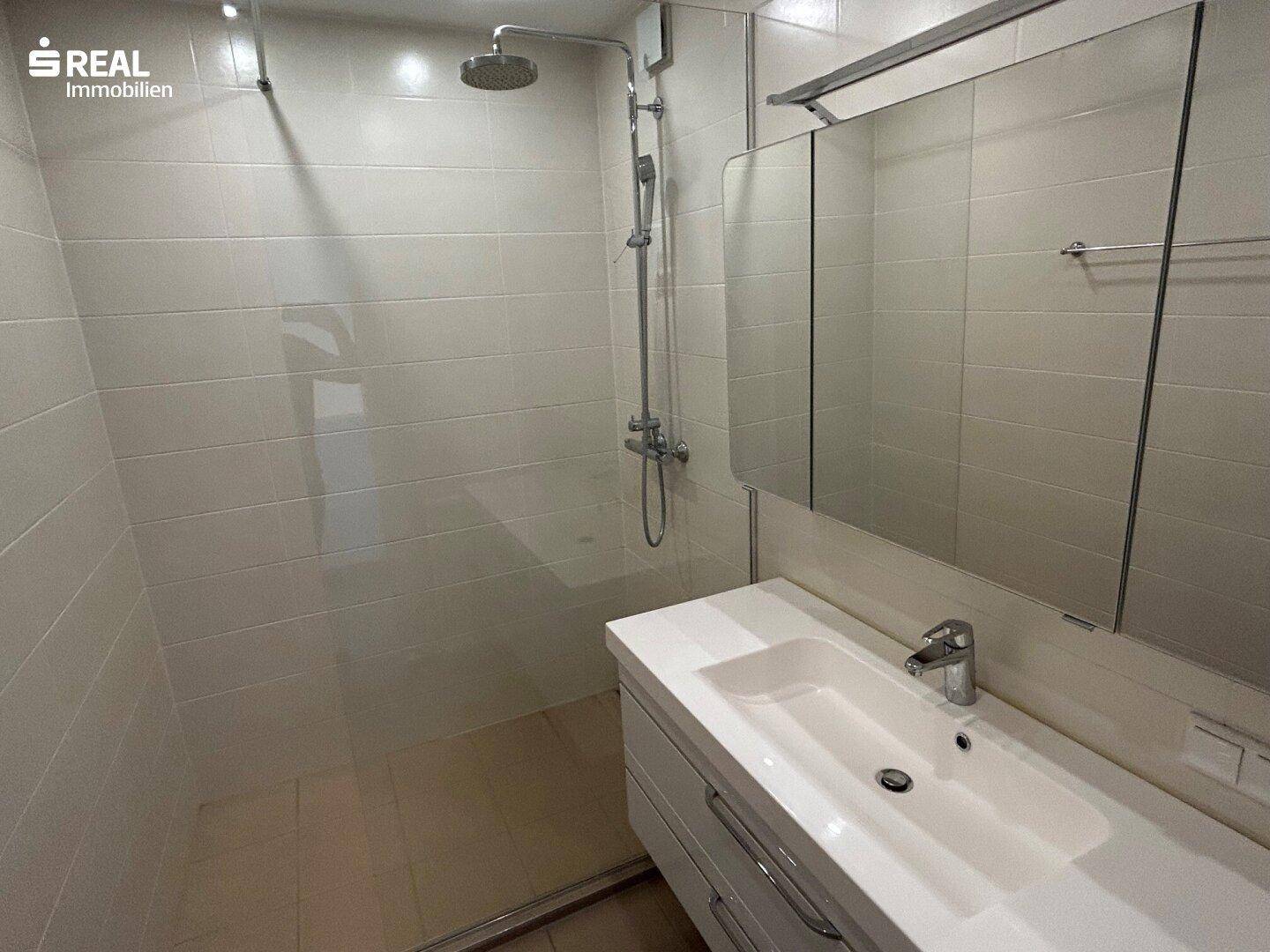 Modernes Badezimmer mit hellen Fliesen, begehbarer Dusche und Waschtisch mit Spiegelschrank.