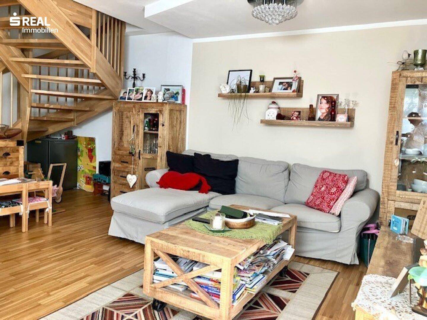 Gemütliches Wohnzimmer mit großem Sofa, Holztisch und offener Holztreppe.