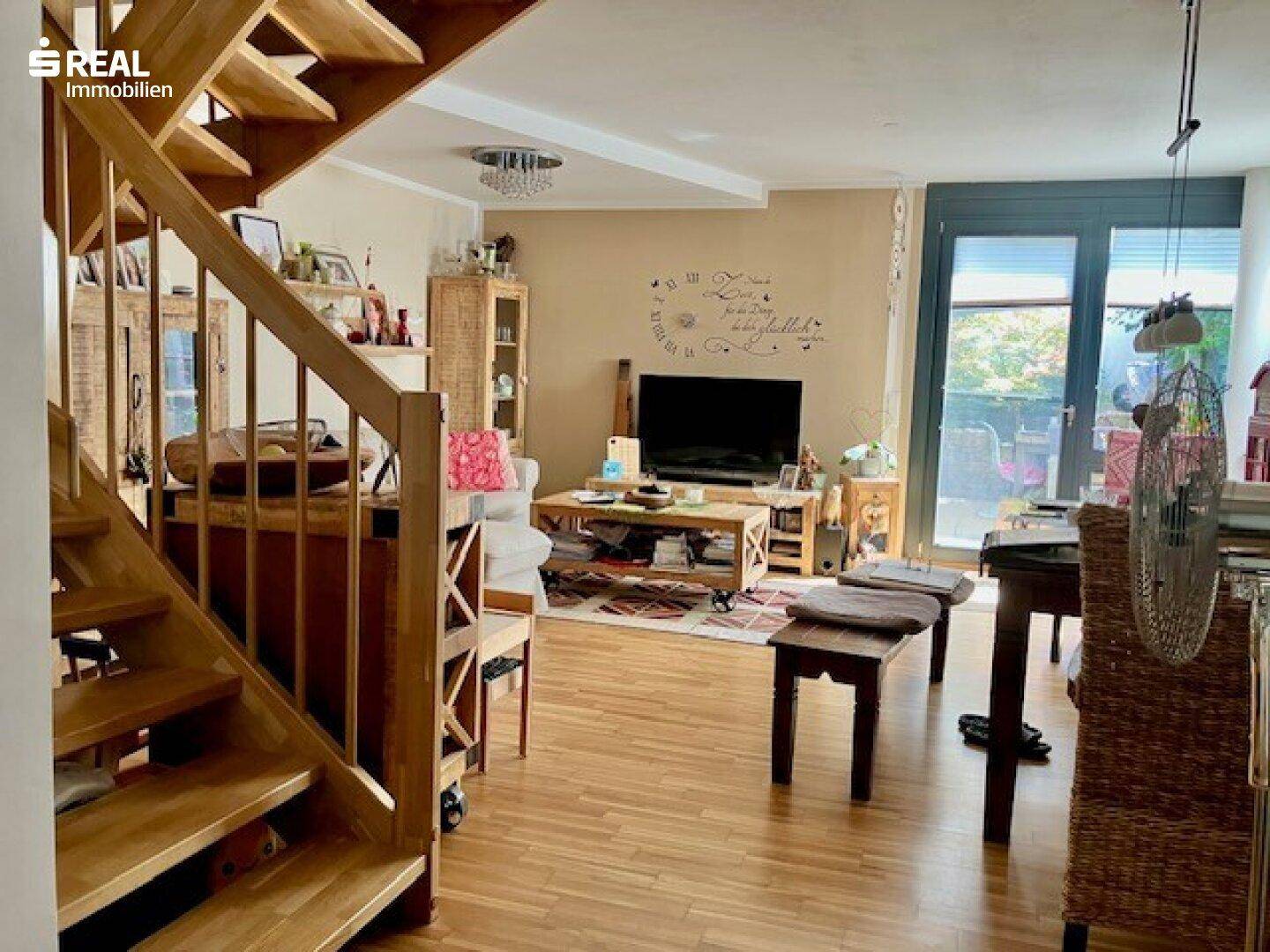 Geräumiges Wohnzimmer mit Holztreppe, Parkettboden und Zugang zur Terrasse.