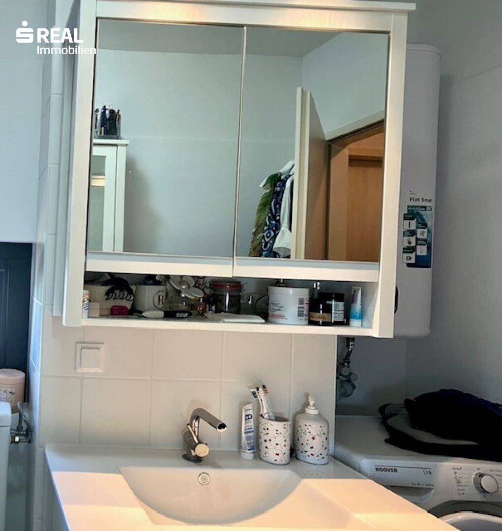 Badezimmer mit Waschbecken, Spiegelschrank und weißer Wandverkleidung.