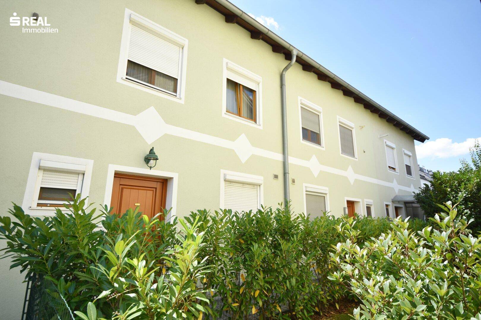Fassade des Hauses mit grüner Bepflanzung und Rollläden an den Fenstern.