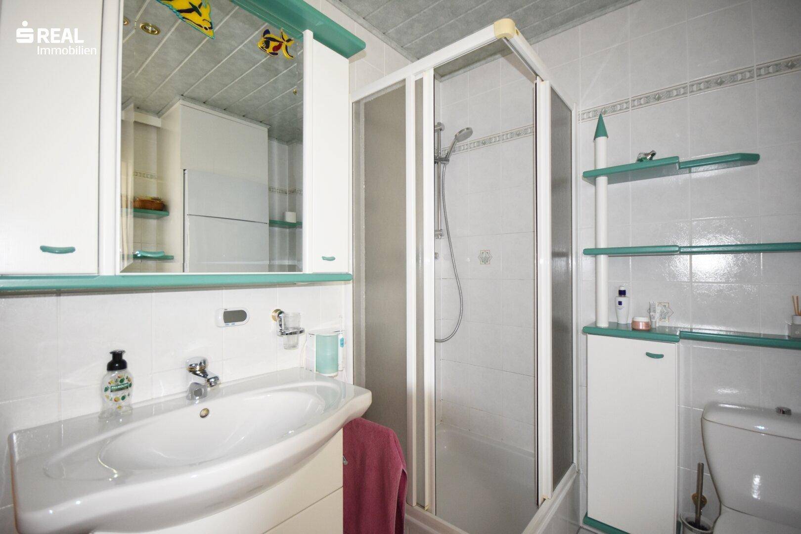Badezimmer mit Dusche, Waschbecken und Spiegelschrank in hellen Farben.