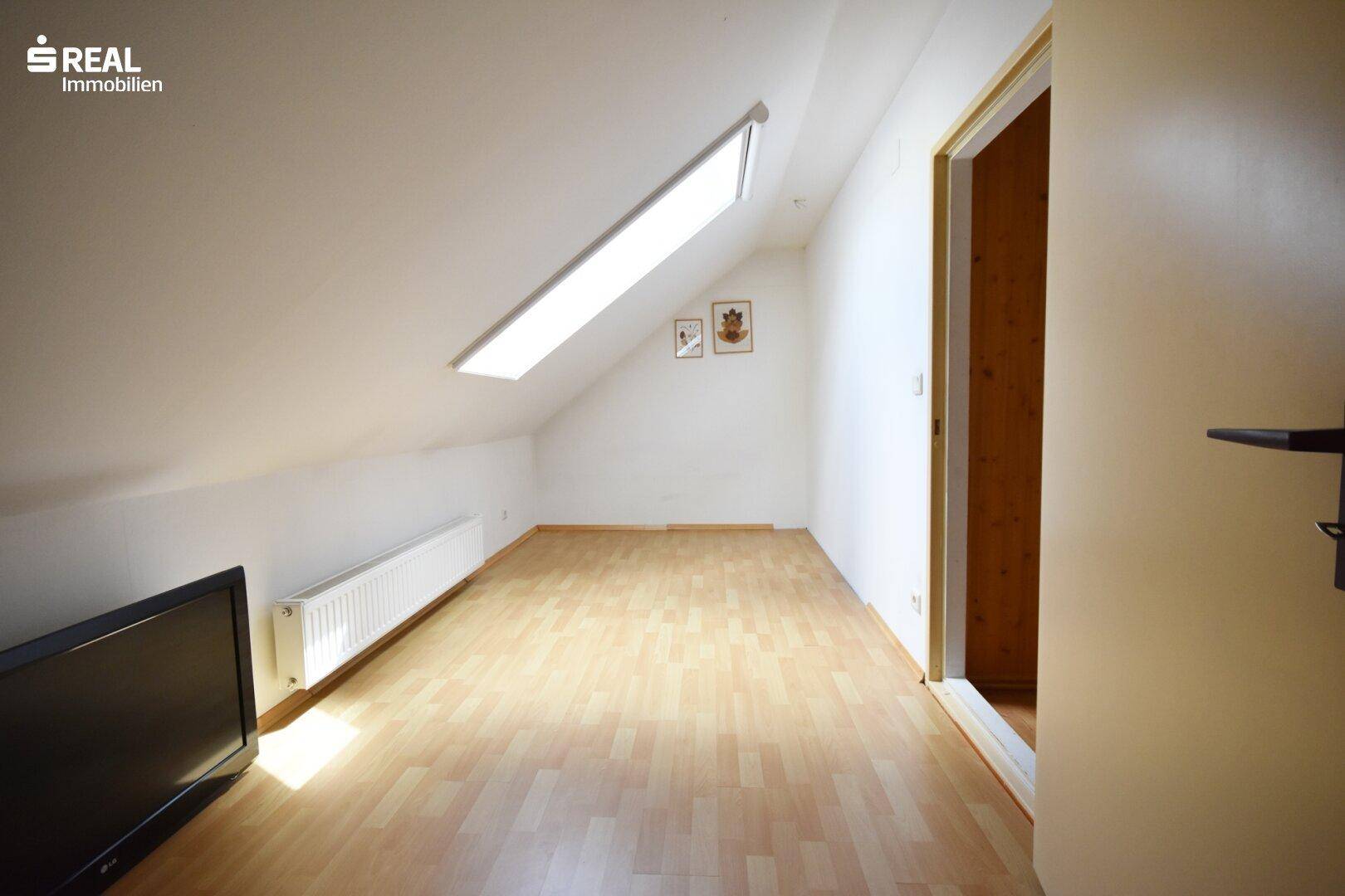 Helles Dachzimmer mit Schrägdach, Laminatboden und Dachfenster.