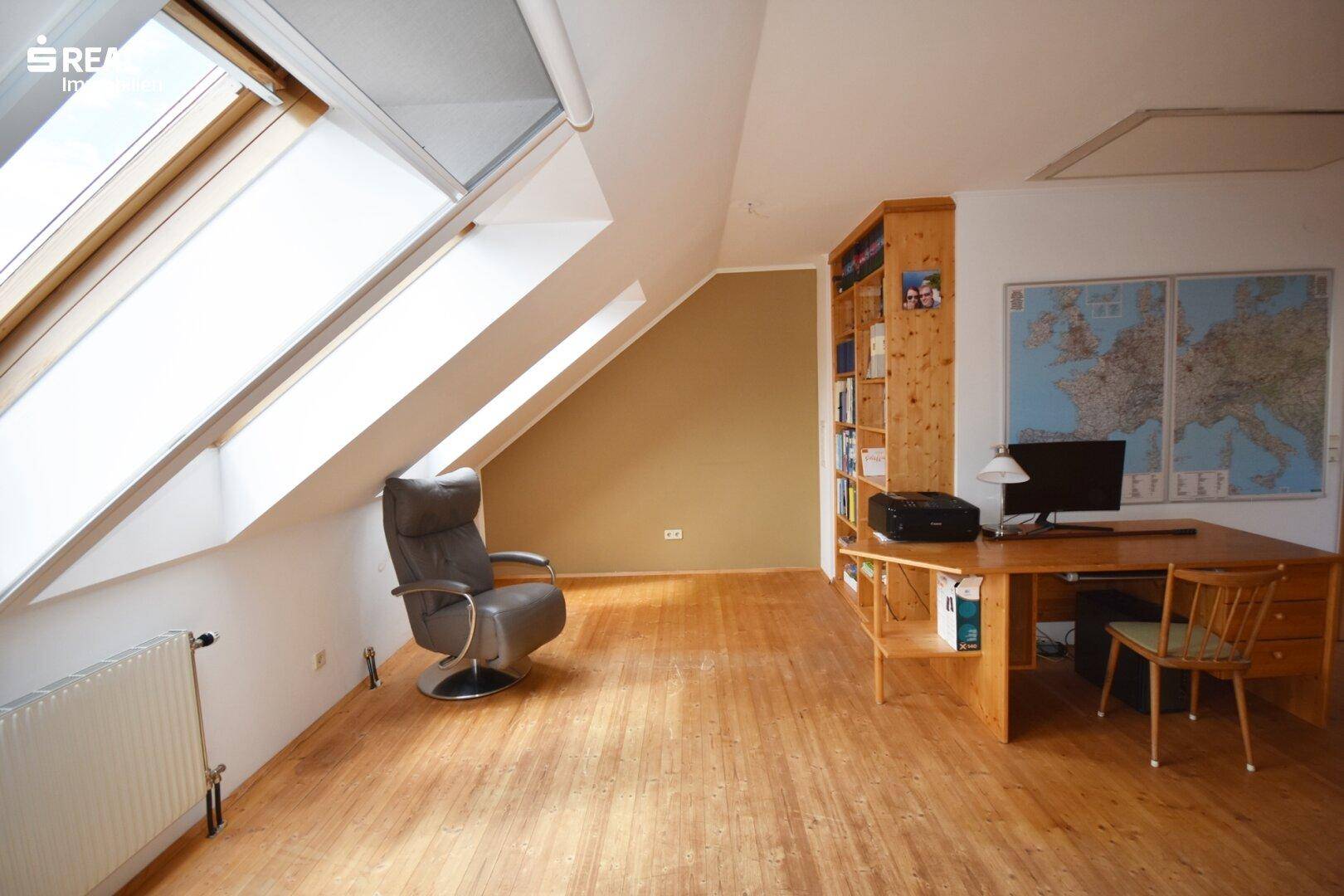 Geräumiges Arbeitszimmer im Dachgeschoss mit Schreibtisch und großen Dachfenstern.
