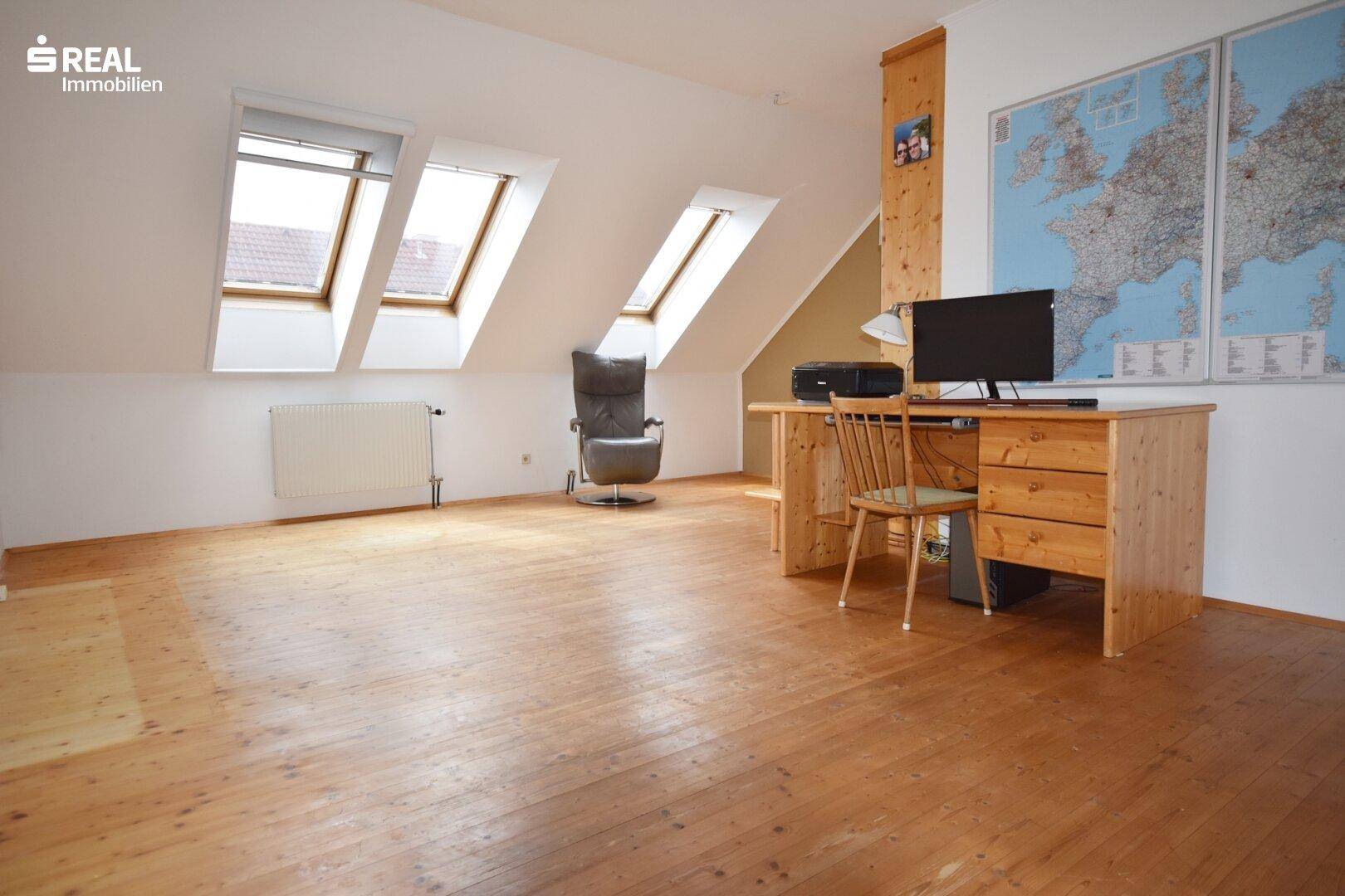 Lichtdurchflutetes Büro im Dachgeschoss mit mehreren Dachfenstern und Holzboden.