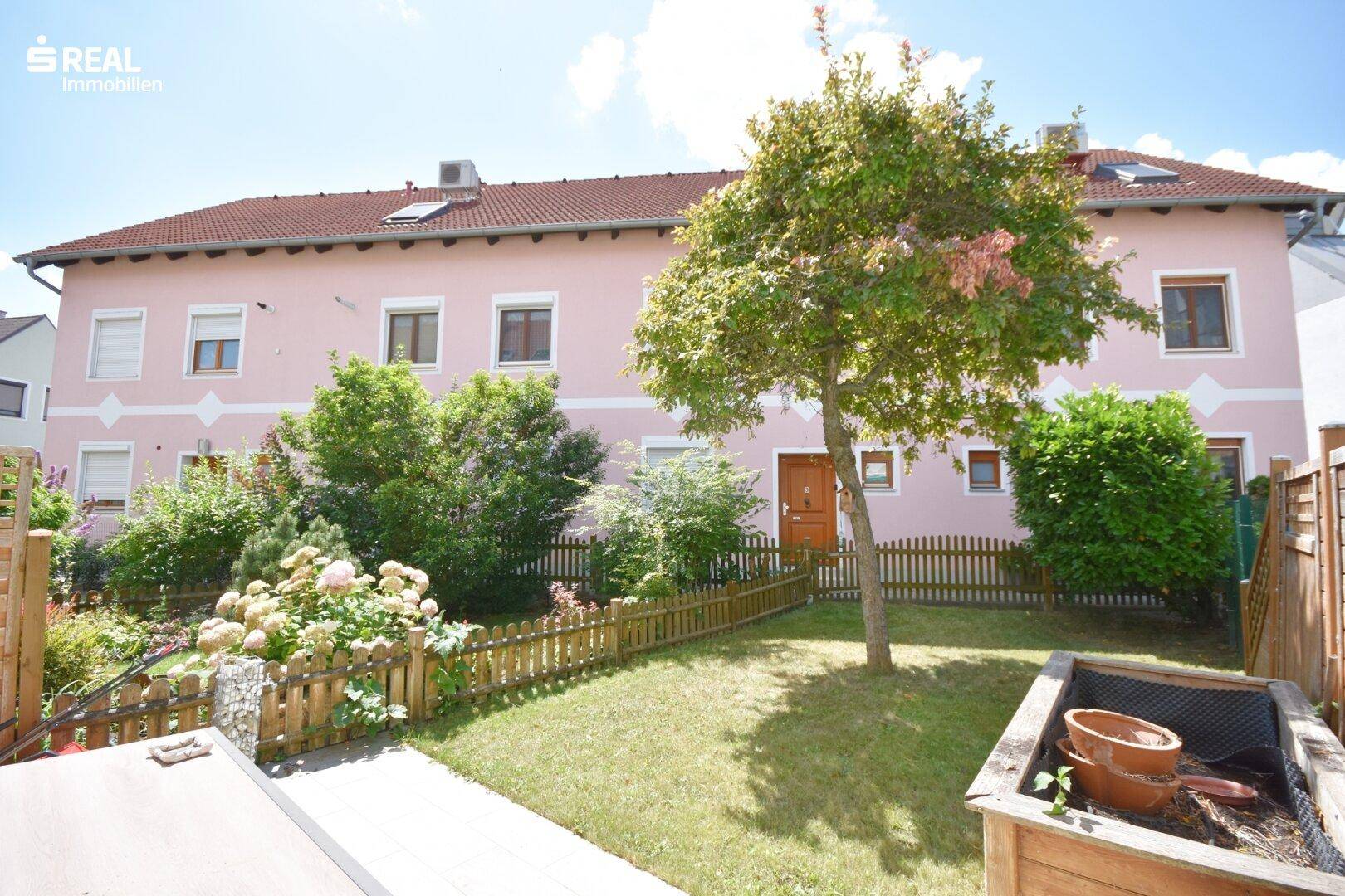 Gepflegter Gartenbereich mit Rasenfläche und blühenden Sträuchern hinter dem Haus.