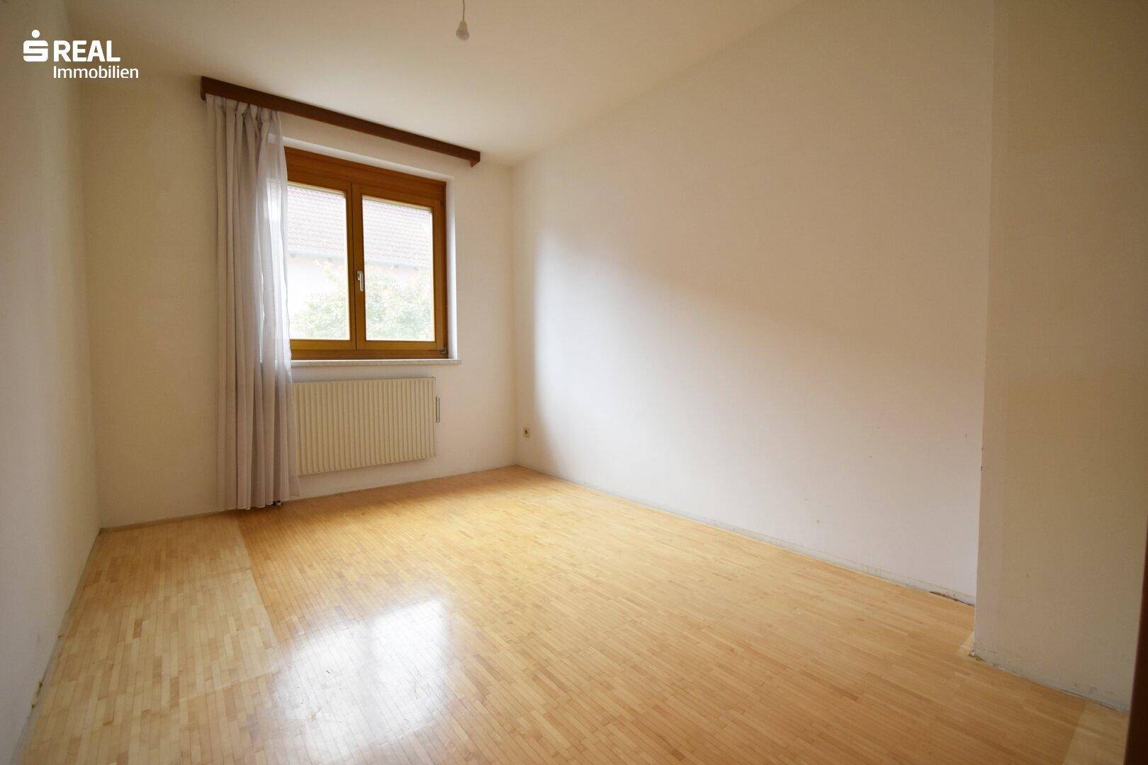 Helles Schlafzimmer mit Parkettboden und großem Fenster.