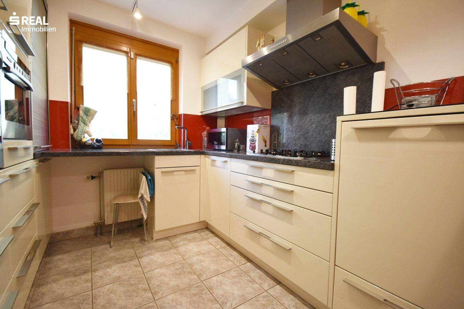 Funktionale Küche mit Fenster, Fliesenboden und integrierten Geräten.