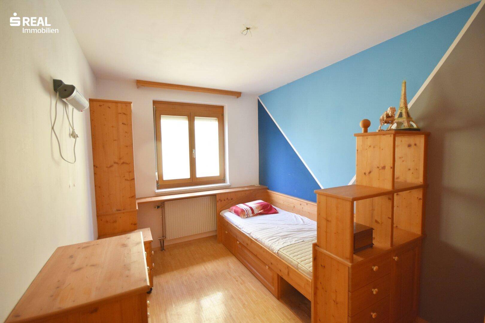 Kinderzimmer mit Holzbett, Schreibtisch und farbiger Wandgestaltung.