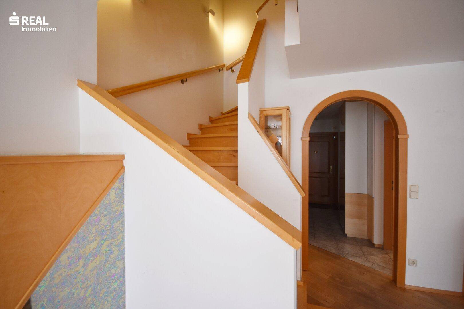 Heller Flur mit Holztreppe und elegantem Rundbogen zum nächsten Bereich.