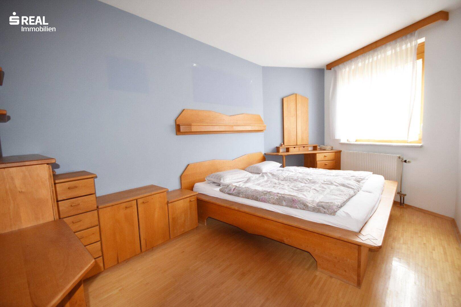 Geräumiges Schlafzimmer mit Holzbett, passenden Möbeln und hellem Parkettboden.