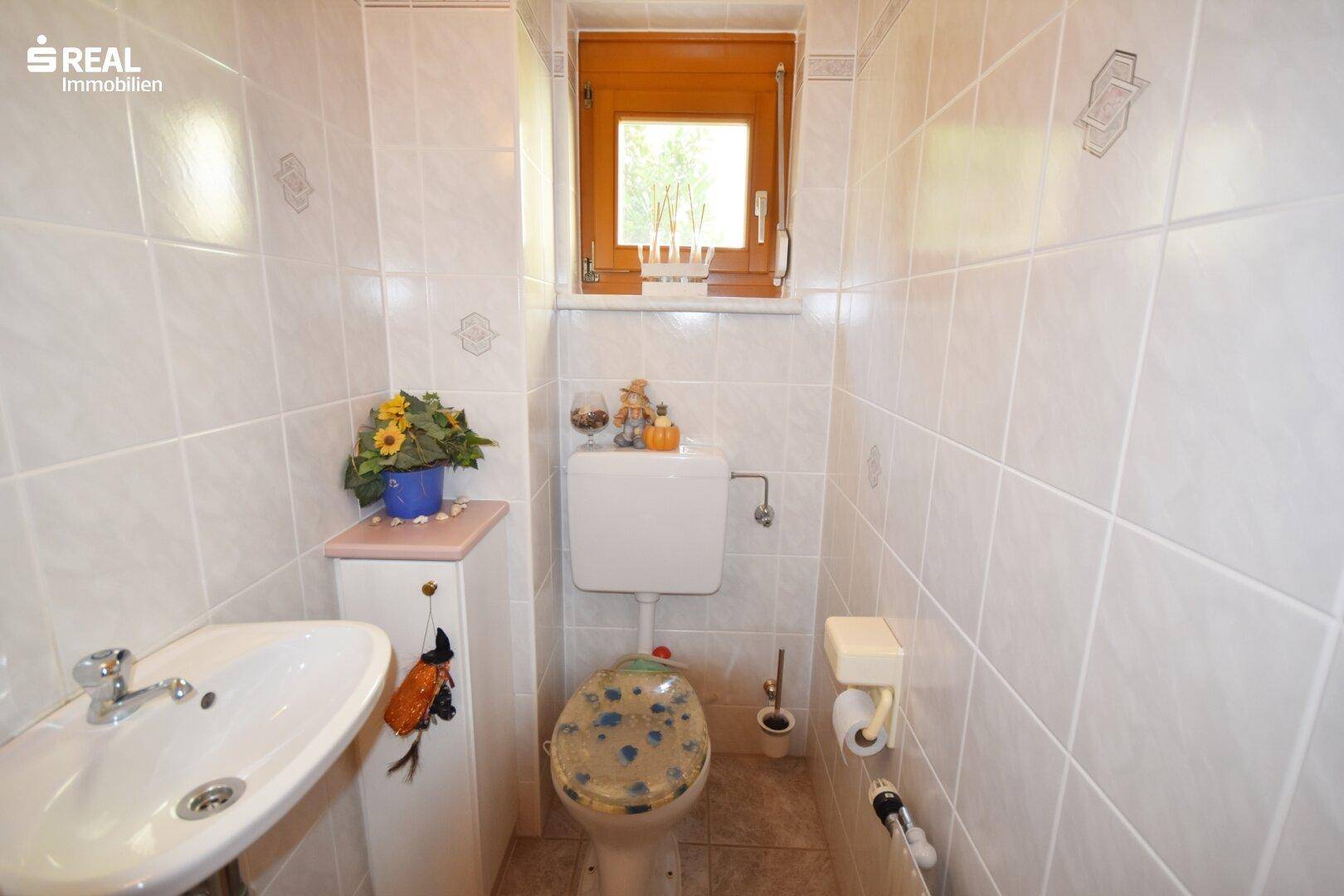 Kleines Gäste-WC mit Waschbecken, Toilette und Fenster.