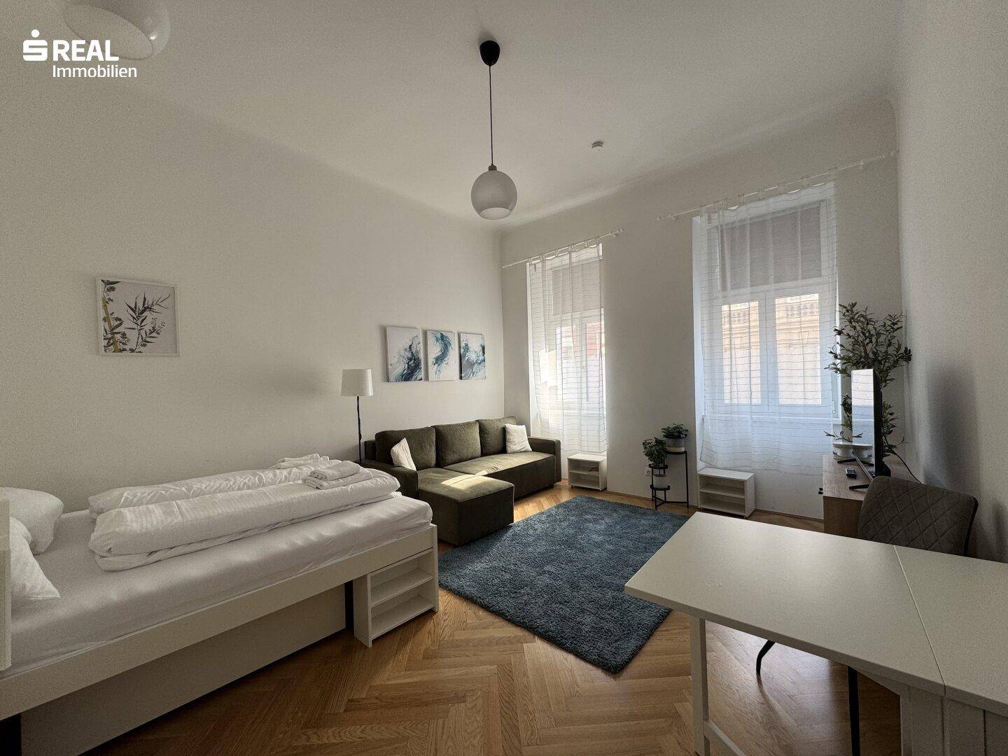 Helles Wohnzimmer mit Parkettboden, Schlafsofa und Esstisch in einem modernen Ambiente.