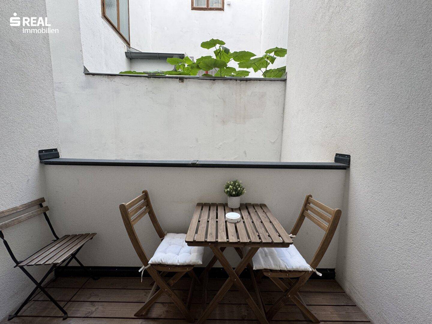 Kleine, private Terrasse mit Holzboden und Sitzgelegenheiten, umgeben von hohen Wänden.