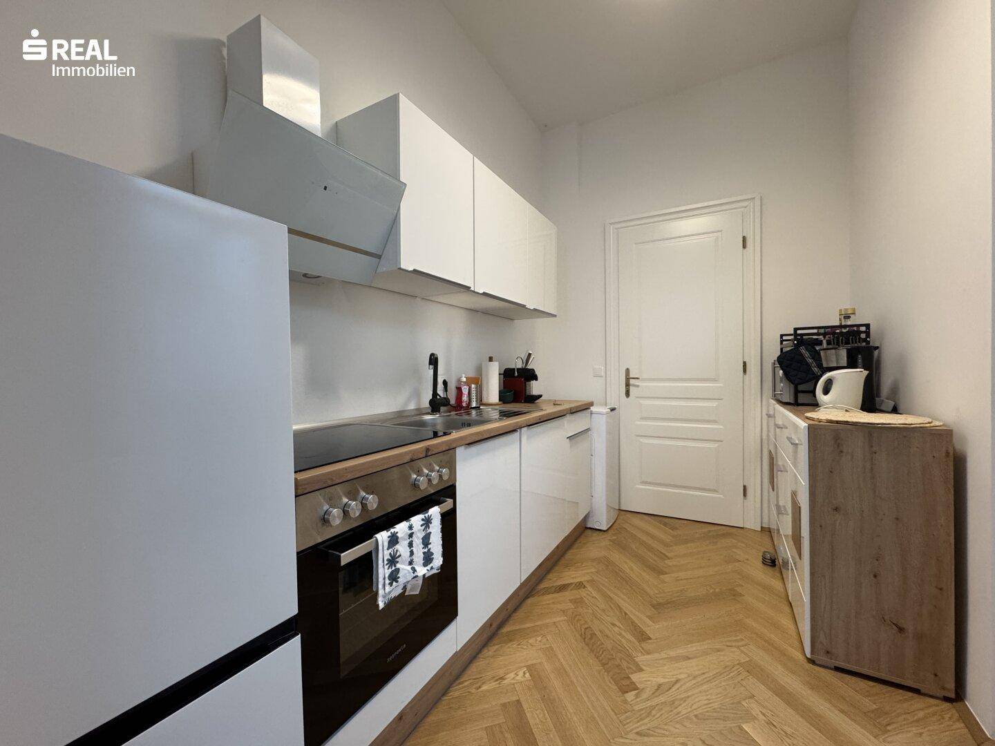Funktionale Küchenzeile mit weißen Schränken, Herd und Kühlschrank, ideal für kleine Wohnungen.