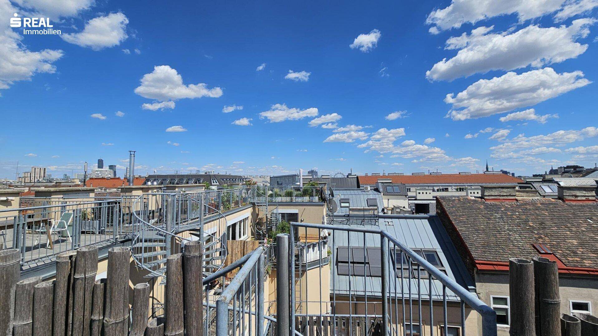 Panoramablick über die Dächer der Stadt mit mehreren Terrassen und blauem Himmel.