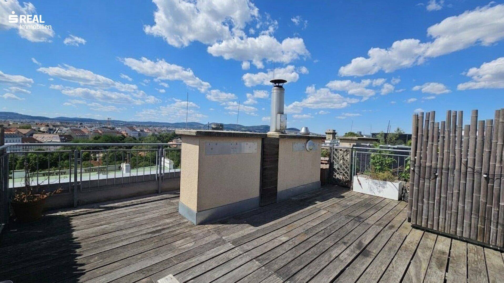 Geräumige Dachterrasse mit Holzboden, gemauertem Grillbereich und weitem Blick über die Stadt.