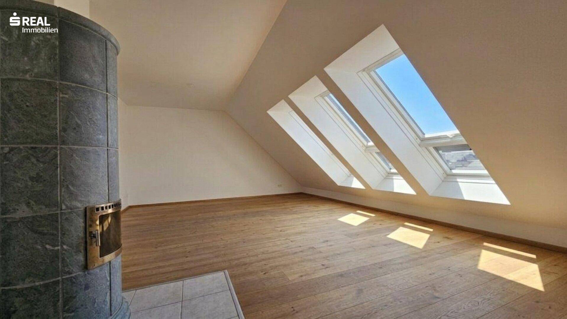 Lichtdurchfluteter Raum im Dachgeschoss mit Holzboden, mehreren Dachfenstern und Kaminofen.