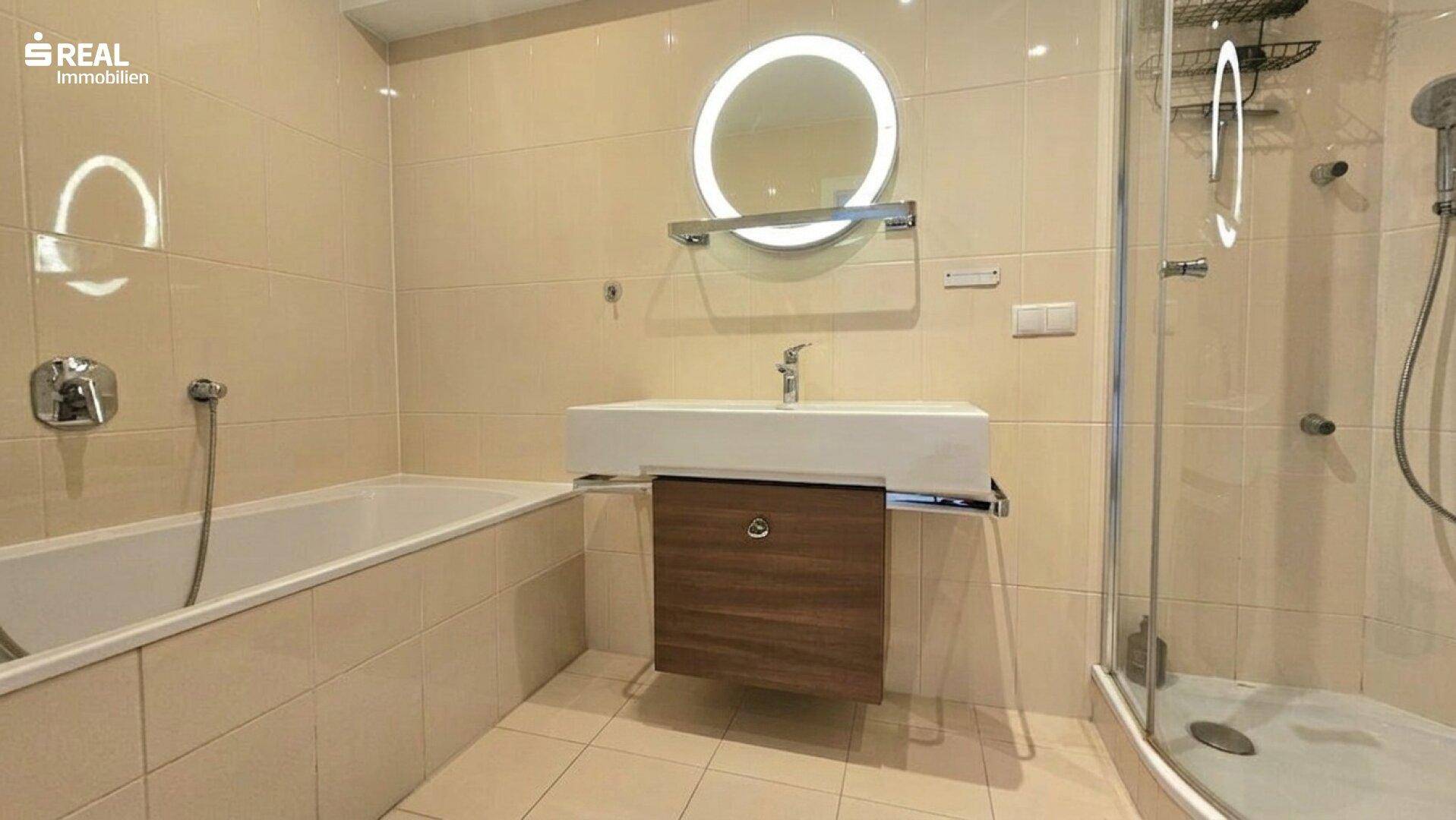Modernes Badezimmer mit Badewanne, Dusche, schwebendem Waschtisch und beleuchtetem Spiegel.