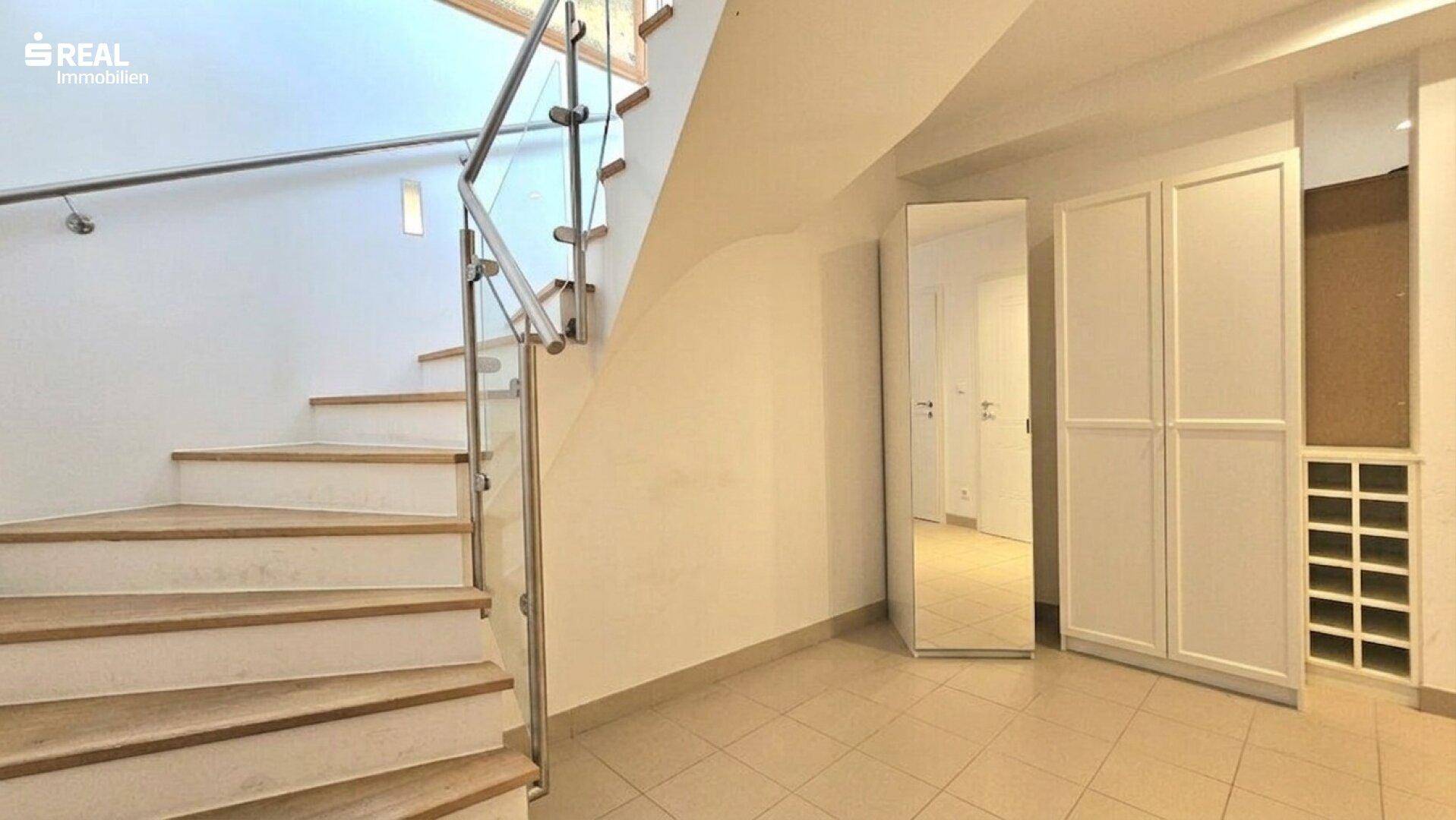 Heller Flur mit Holztreppe, Glasgeländer und integrierten Schränken für Stauraum.