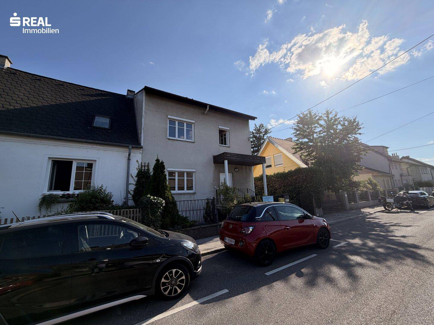 Ansicht des Hauses von der Straße mit parkenden Autos und sonnigem Wetter.