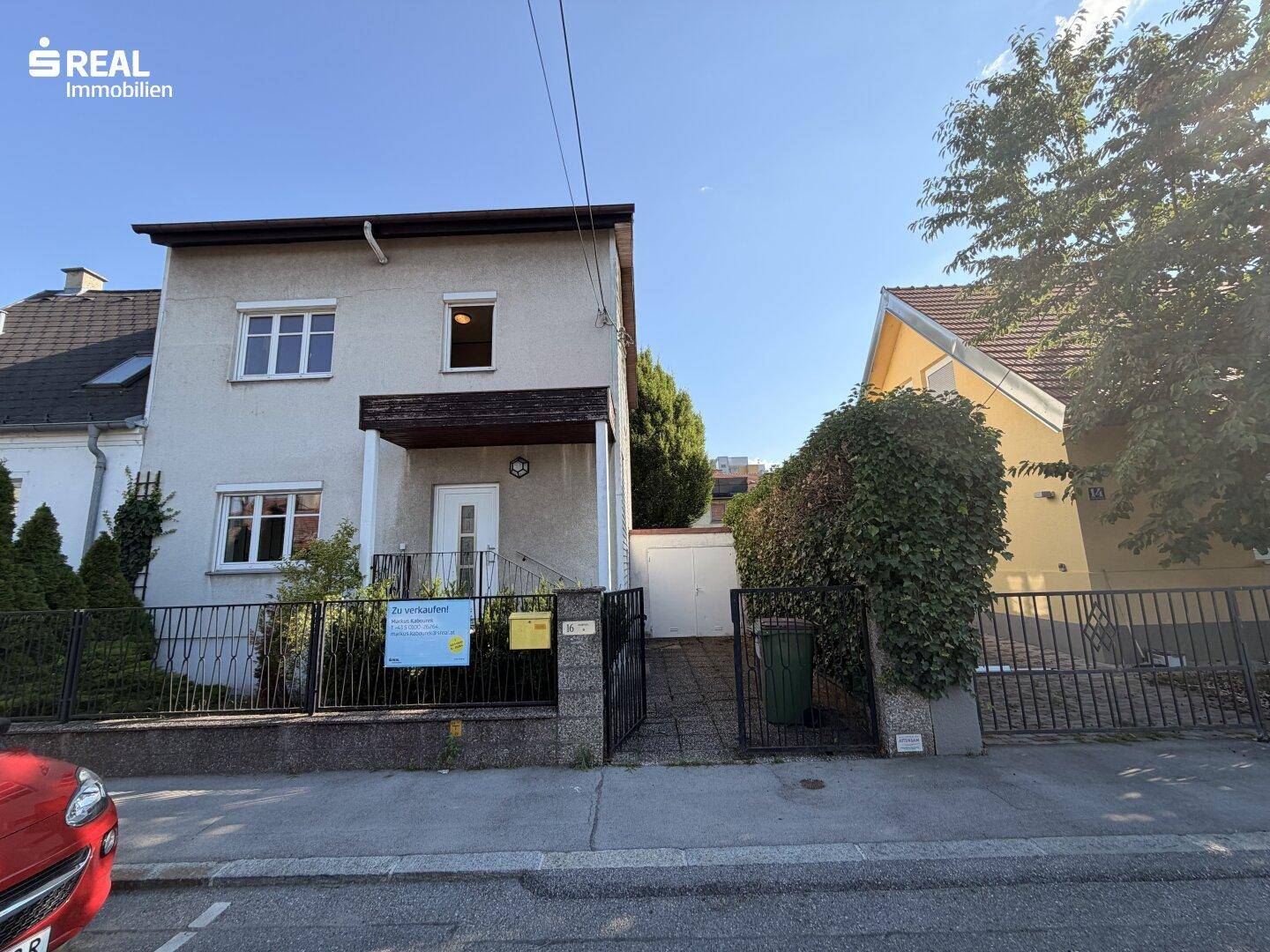 Frontansicht des Einfamilienhauses mit Vorgarten, Zaun und Zufahrt bei klarem Himmel.