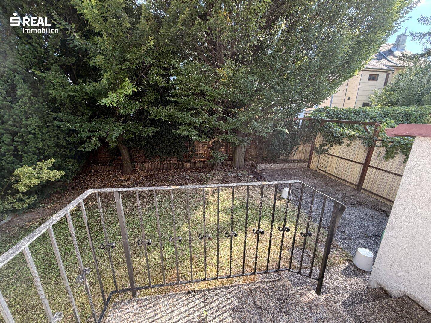 Kleiner Gartenbereich mit Rasenfläche, Bäumen und Blick auf die Rückseite des Hauses.