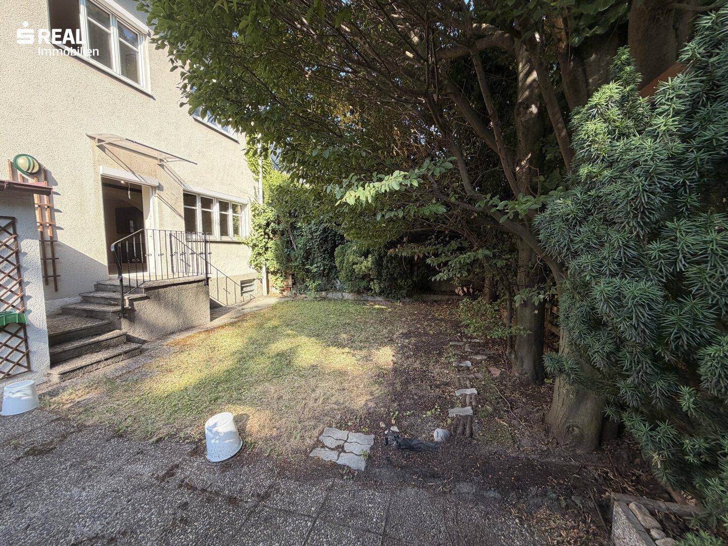 Gepflegter Gartenbereich hinter dem Haus mit Rasen und altem Baumbestand.