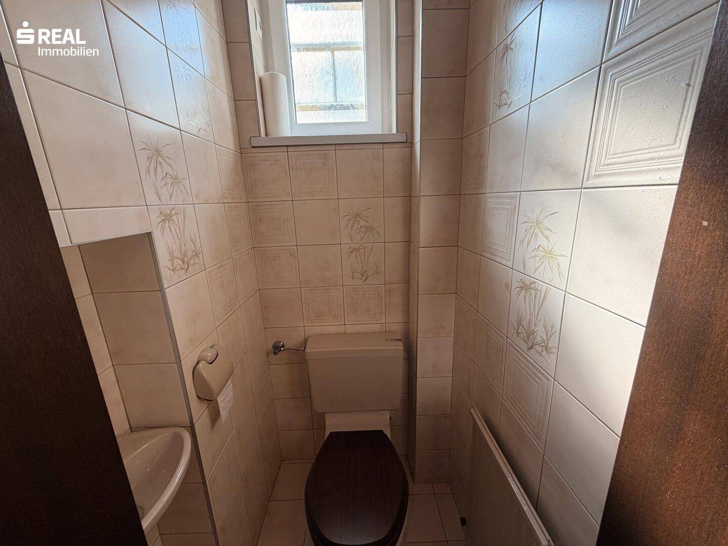 Kleines Gäste-WC mit Fliesenboden, Fenster und Wandfliesen mit Muster.