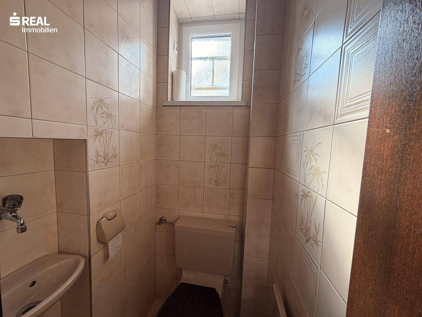 Gäste-WC mit Waschbecken, Toilette und Fenster für natürliche Belüftung.