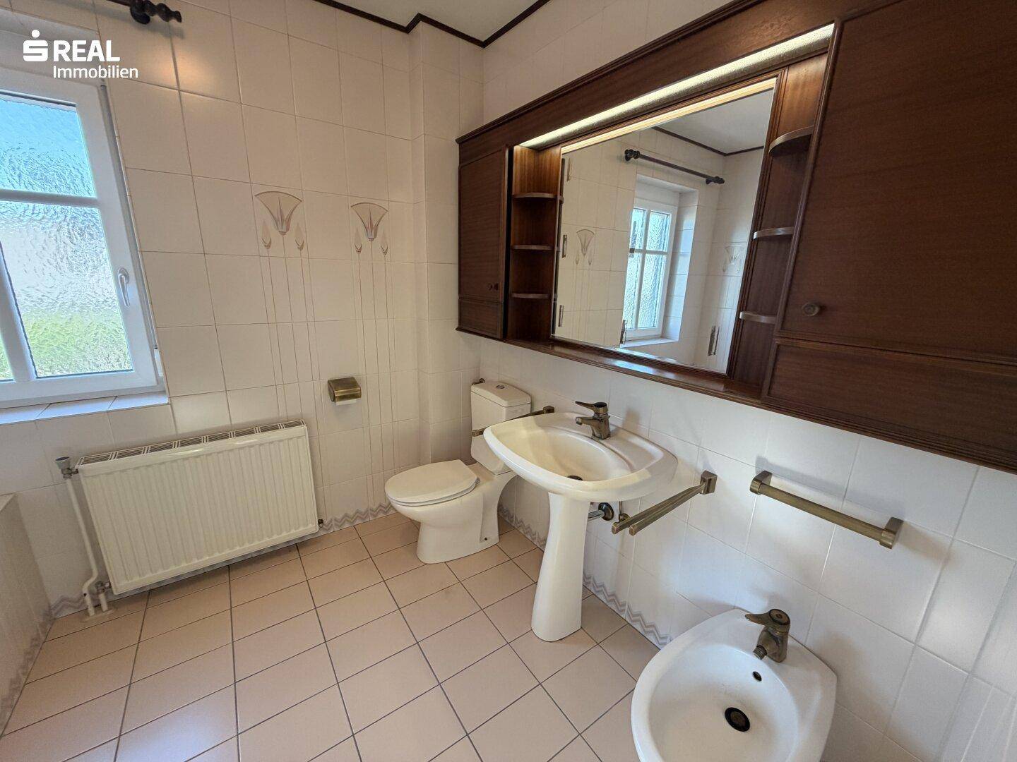Badezimmer mit Fliesen, Fenster, Waschtisch, Toilette und Bidet.