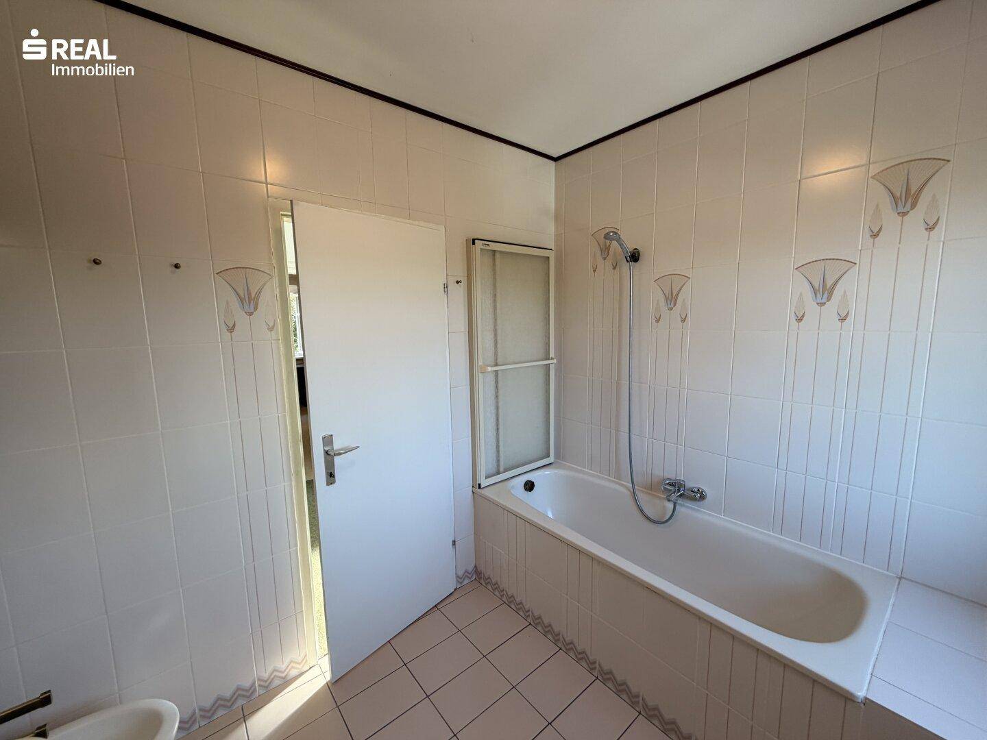 Badezimmer mit Badewanne, Duschvorrichtung und hellen Wandfliesen.