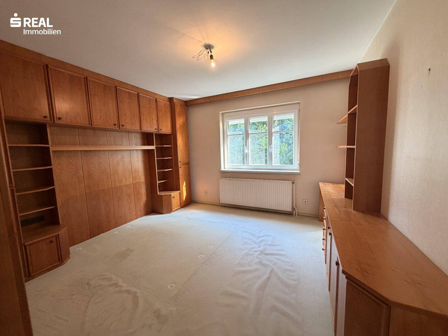 Geräumiges Schlafzimmer mit hellen Holzschränken, Teppichboden und einem großen Fenster.