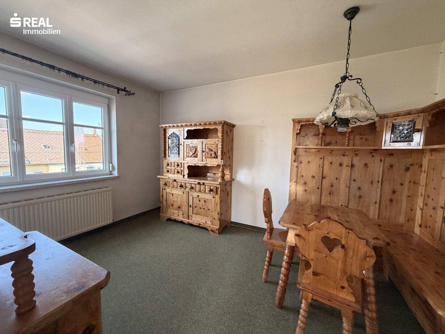 Gemütlicher Essbereich im alpinen Stil mit rustikalen Holzmöbeln, grüner Auslegware und Fenster.