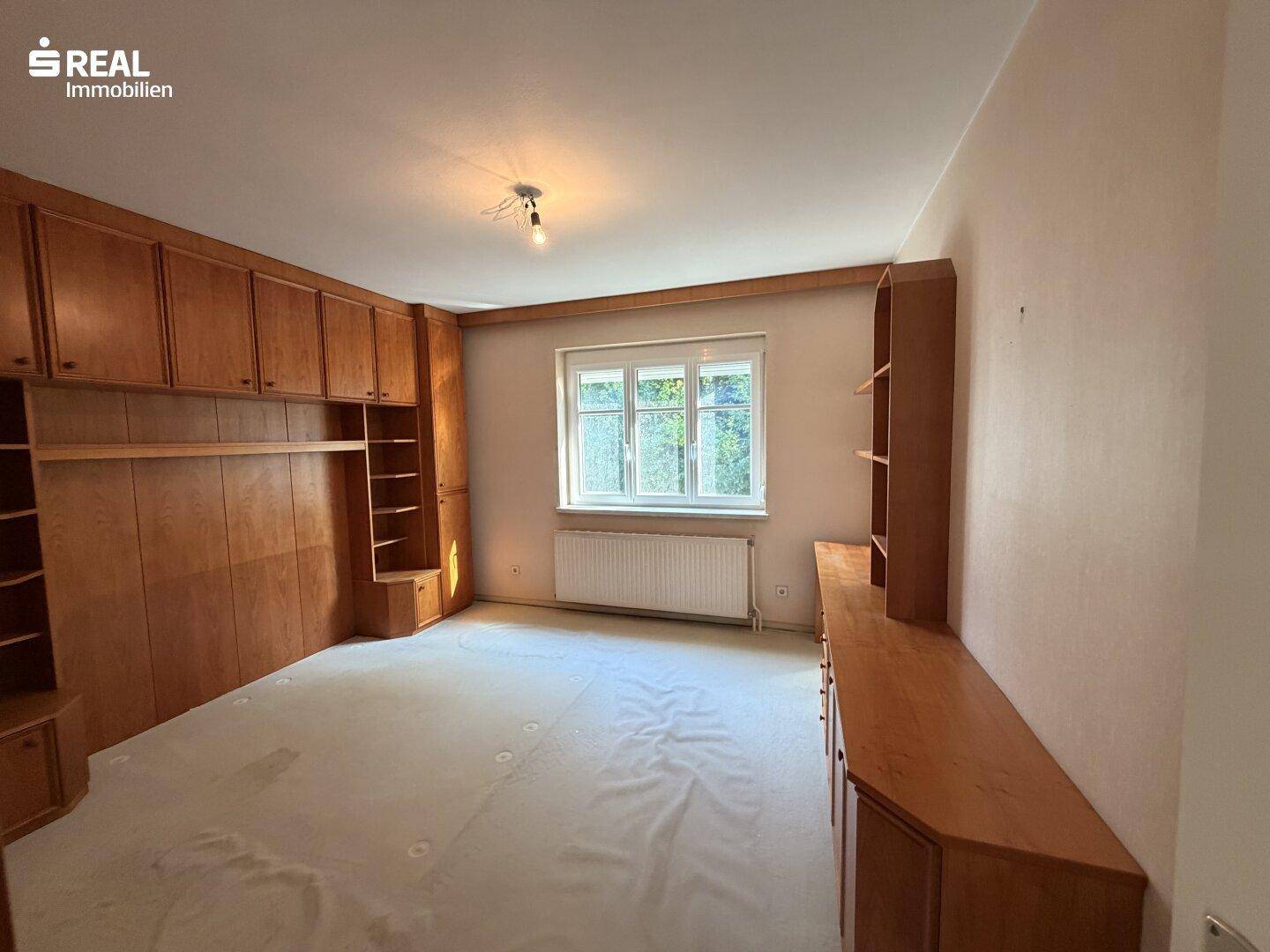 Schlafzimmer mit hellen Holzmöbeln, Teppichboden und einem Fenster, das viel Licht spendet.