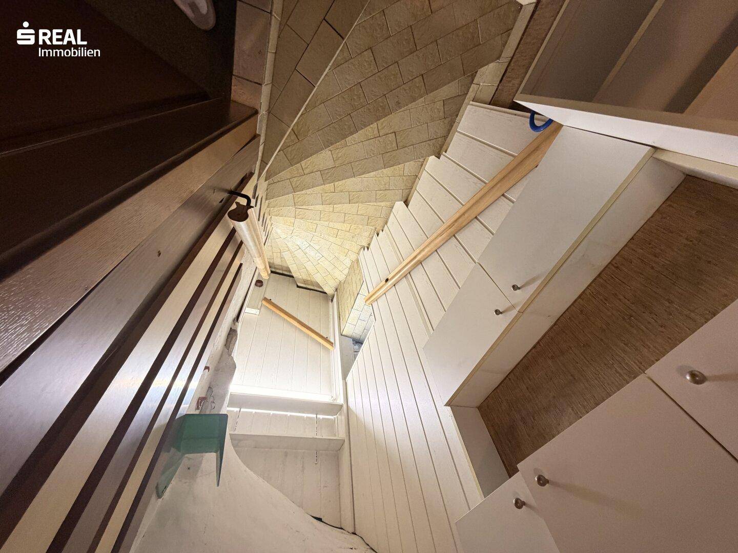Wendeltreppe mit Holzstufen und weiß getäfelten Wänden, die ein helles Ambiente schaffen.