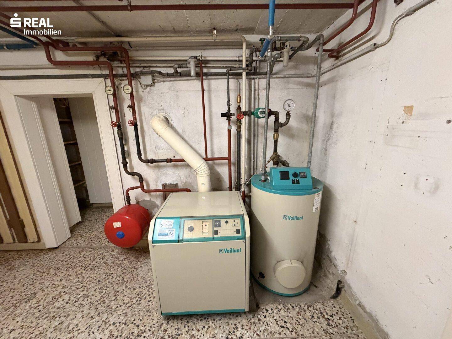 Heizungsraum im Keller mit Heizkessel, Warmwasserspeicher und sichtbaren Rohren.