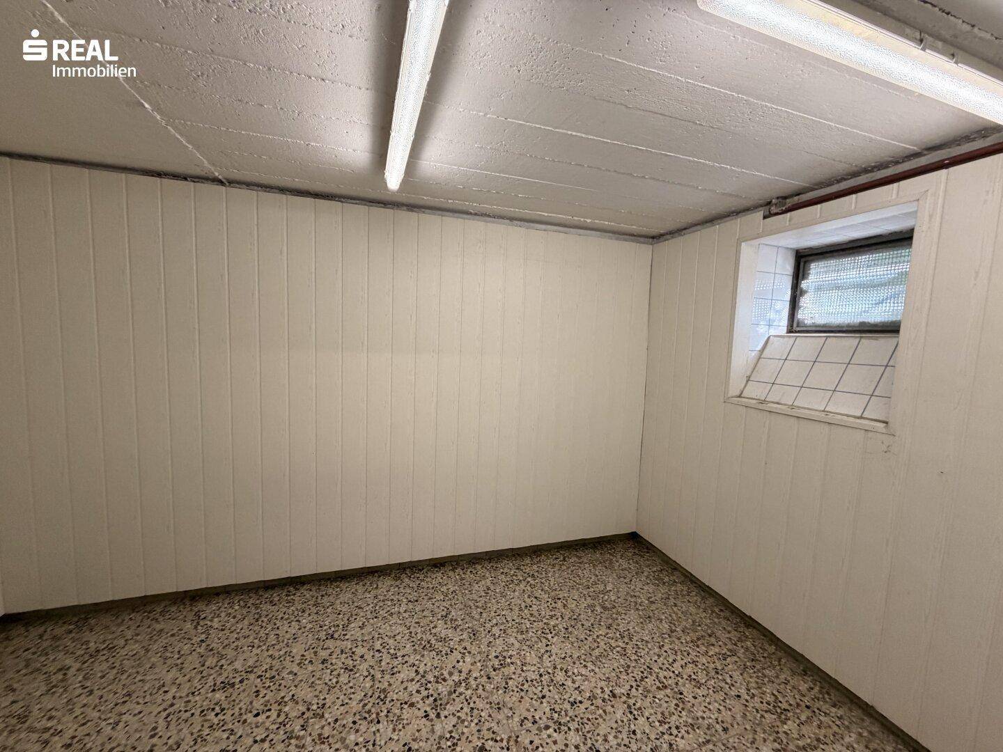 Kellerraum mit weiß getäfelten Wänden, kleinem Fenster und Terrazzoboden.