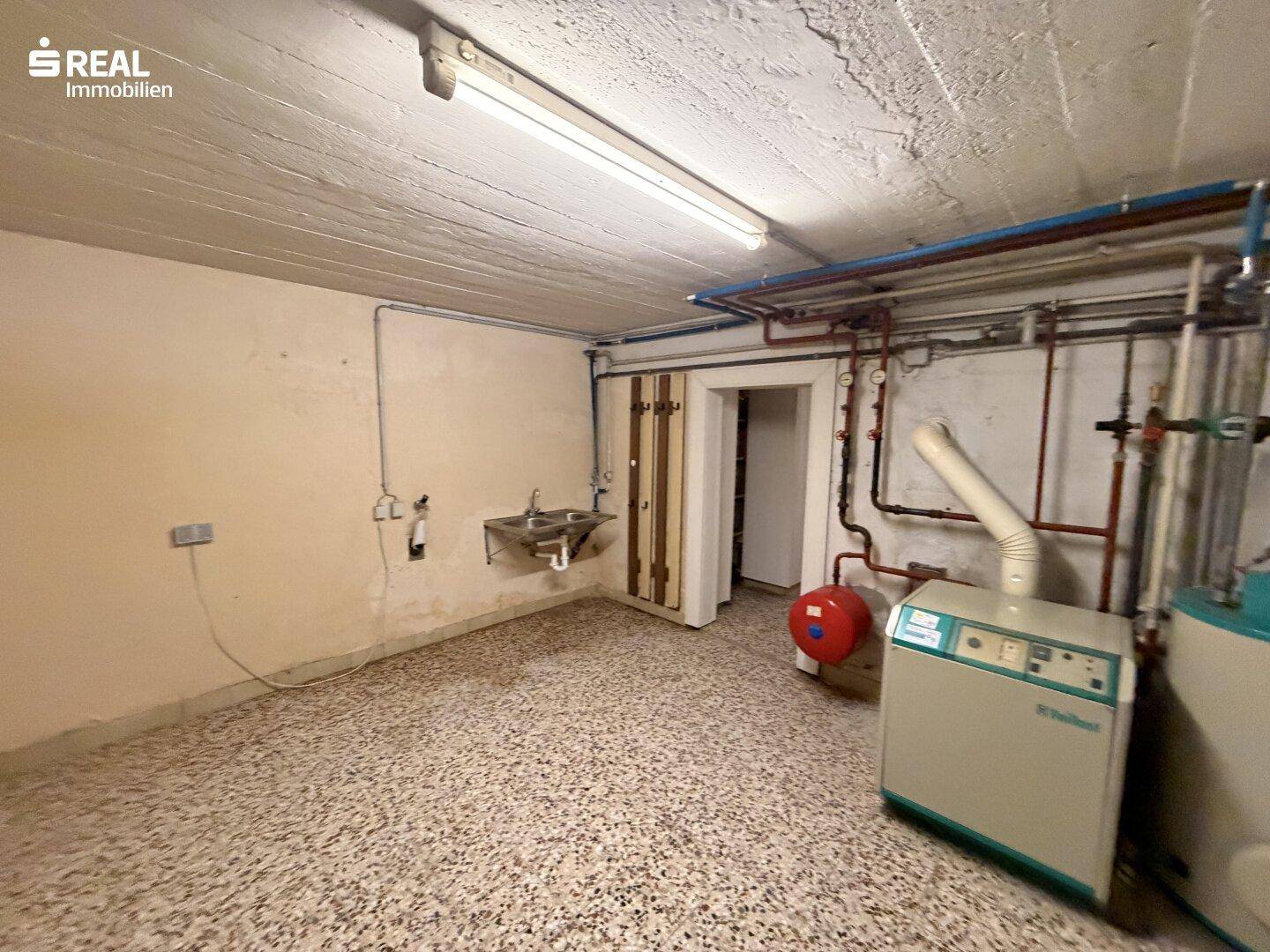 Hauswirtschaftsraum im Keller mit Heizungsanlage, Waschbecken und sichtbaren Leitungen.