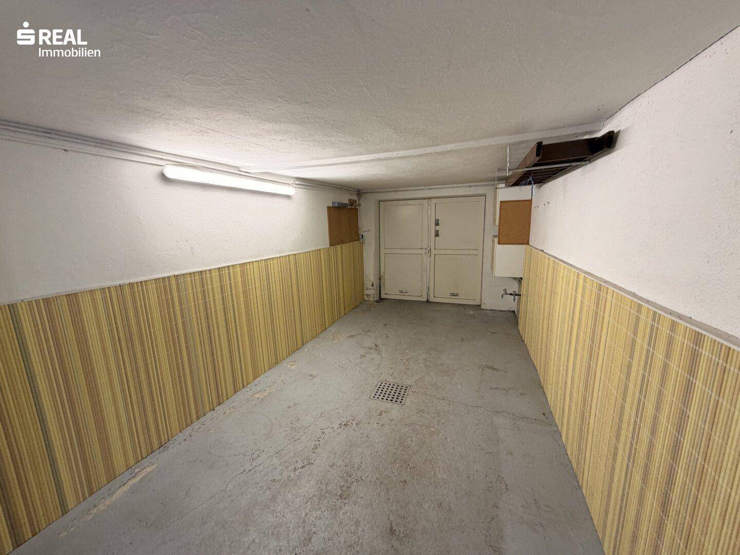 Geräumige Garage mit Betonboden und gestreiften Wandpaneelen, bietet viel Platz.