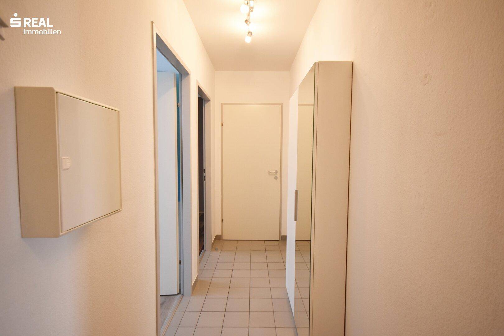 Heller Flur mit Fliesenboden und weiß gestrichenen Wänden.