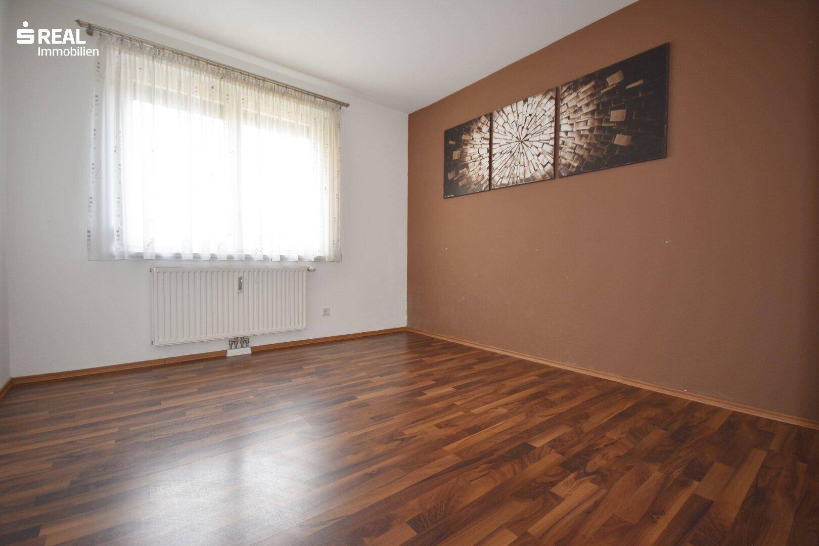 Schlafzimmer mit dunklem Laminatboden und einer braunen Akzentwand.