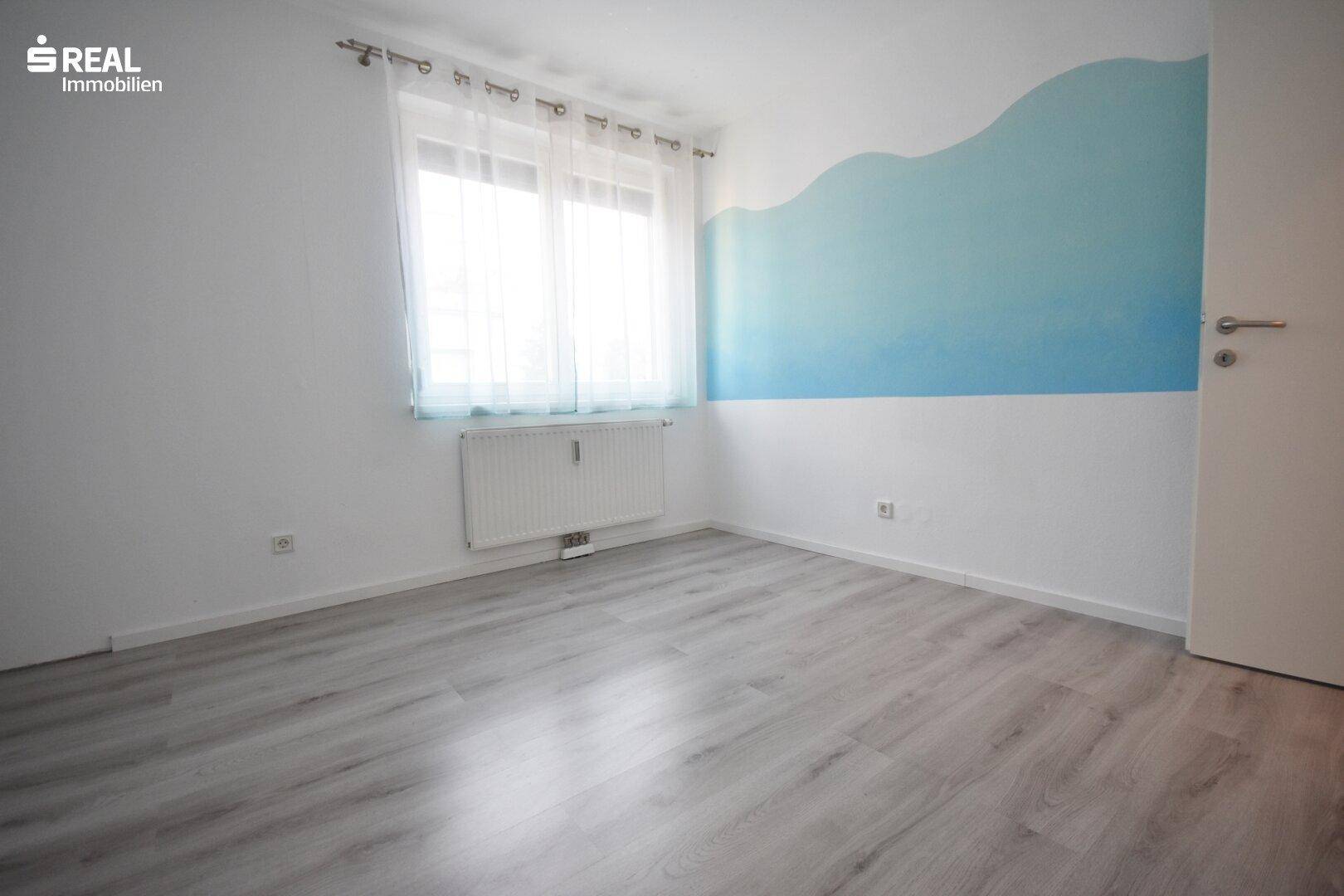 Helles Schlafzimmer mit hellem Laminatboden und einer blauen Akzentwand.