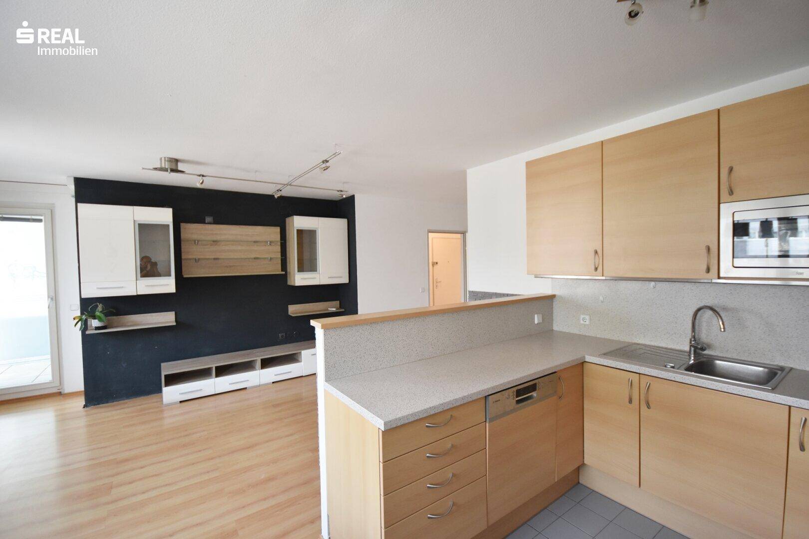 Offener Wohnbereich mit integrierter Küche, Holzboden und Zugang zum Balkon.