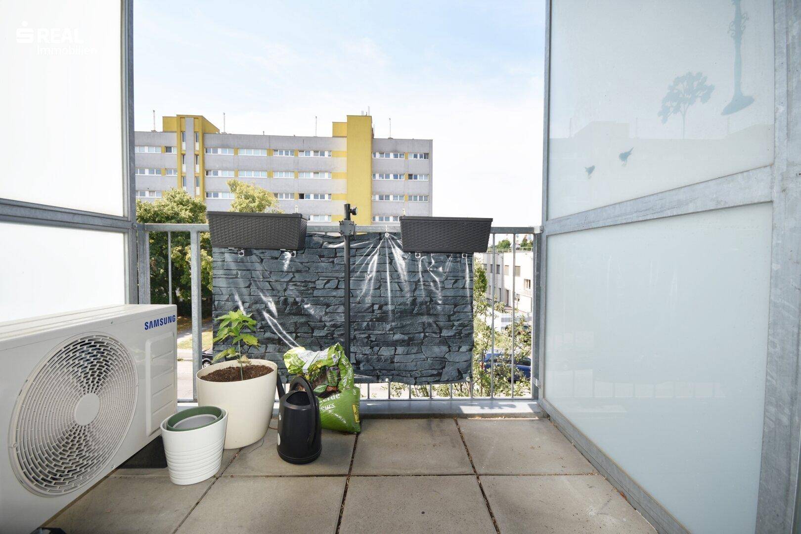 Balkon mit Fliesenboden, Klimaanlage und Blick auf die Umgebung.