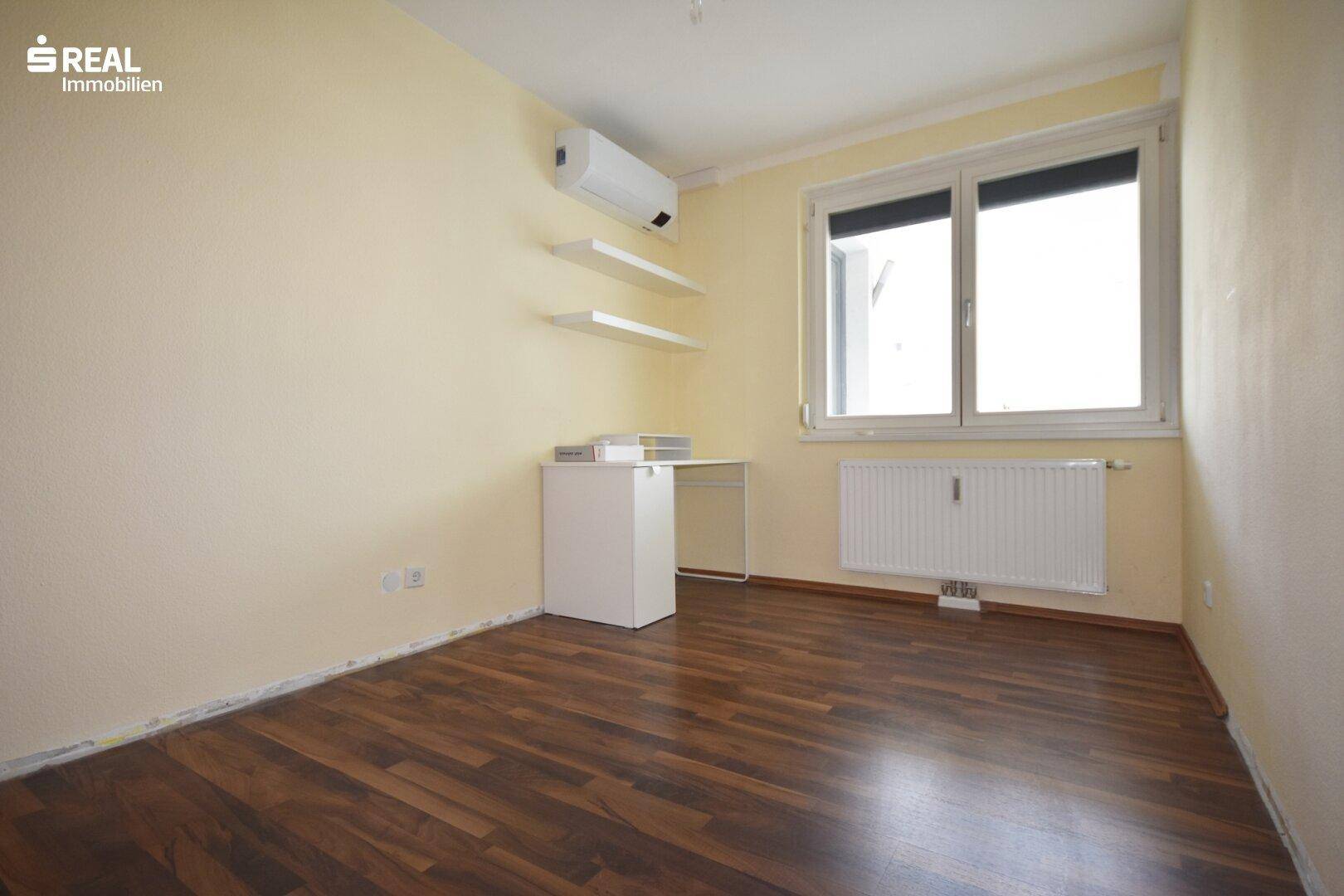 Arbeitszimmer mit dunklem Laminatboden, Klimaanlage und Fenster.