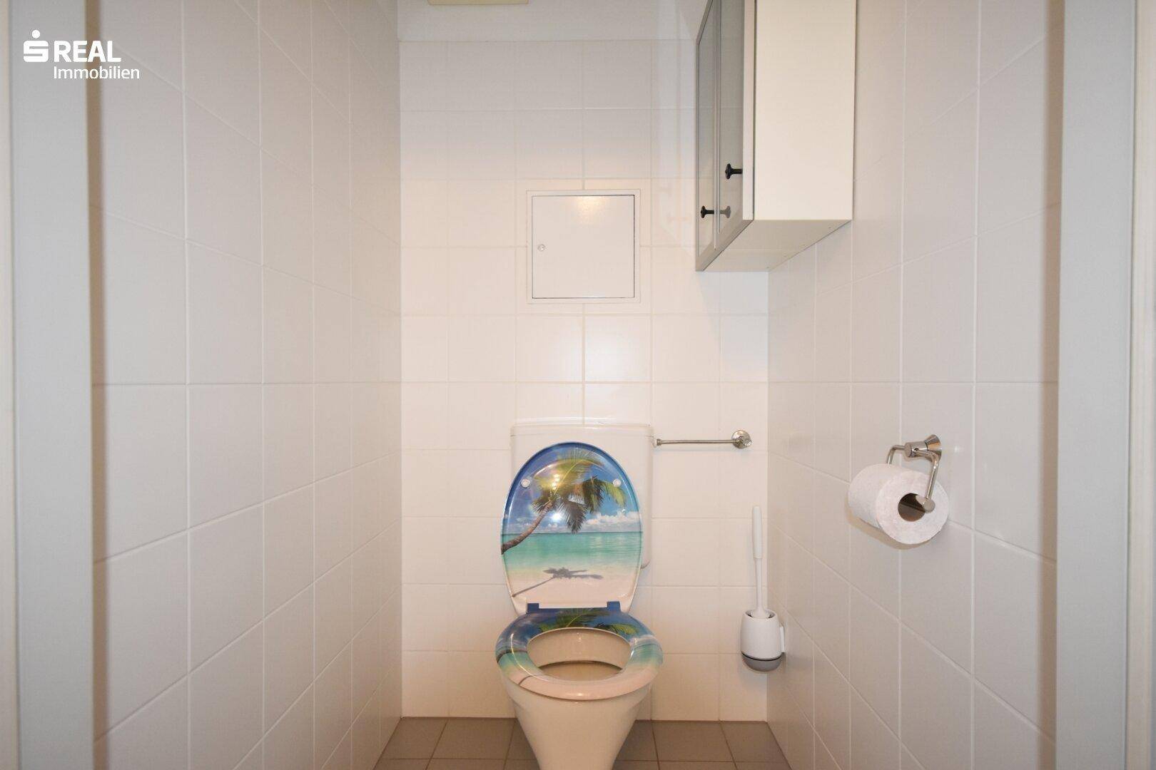 Separate Toilette mit Fliesenboden und einer dekorativen Toilettenbrille.