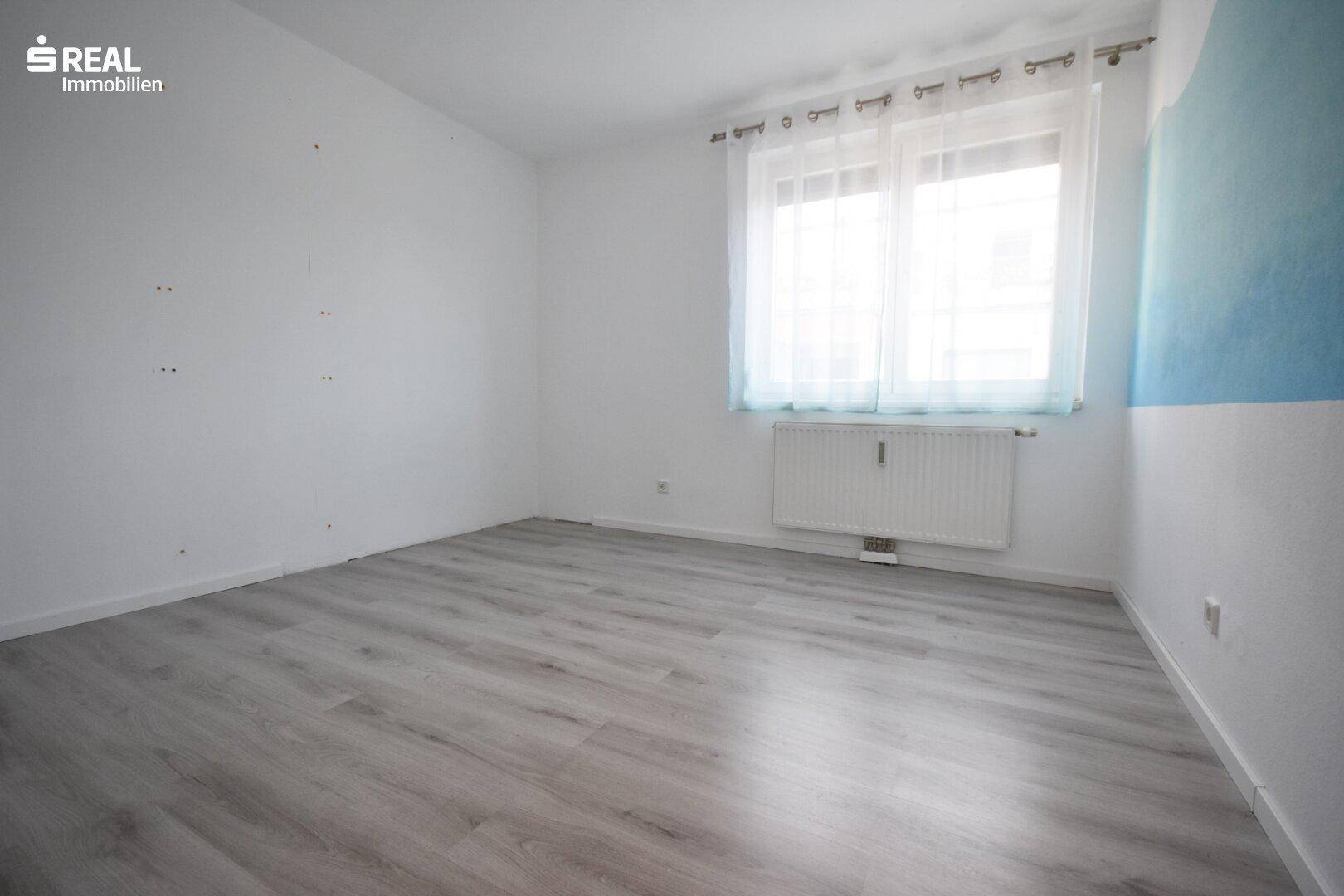Geräumiges Schlafzimmer mit hellem Laminatboden und großen Fenstern.
