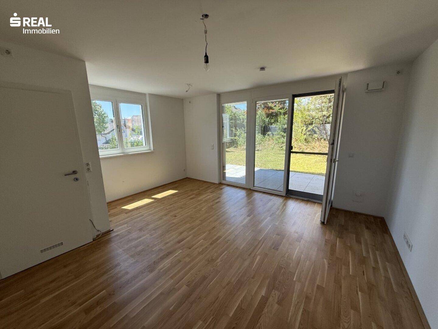 Heller, leerer Raum mit Holzboden und direktem Zugang zur Terrasse und zum Garten.