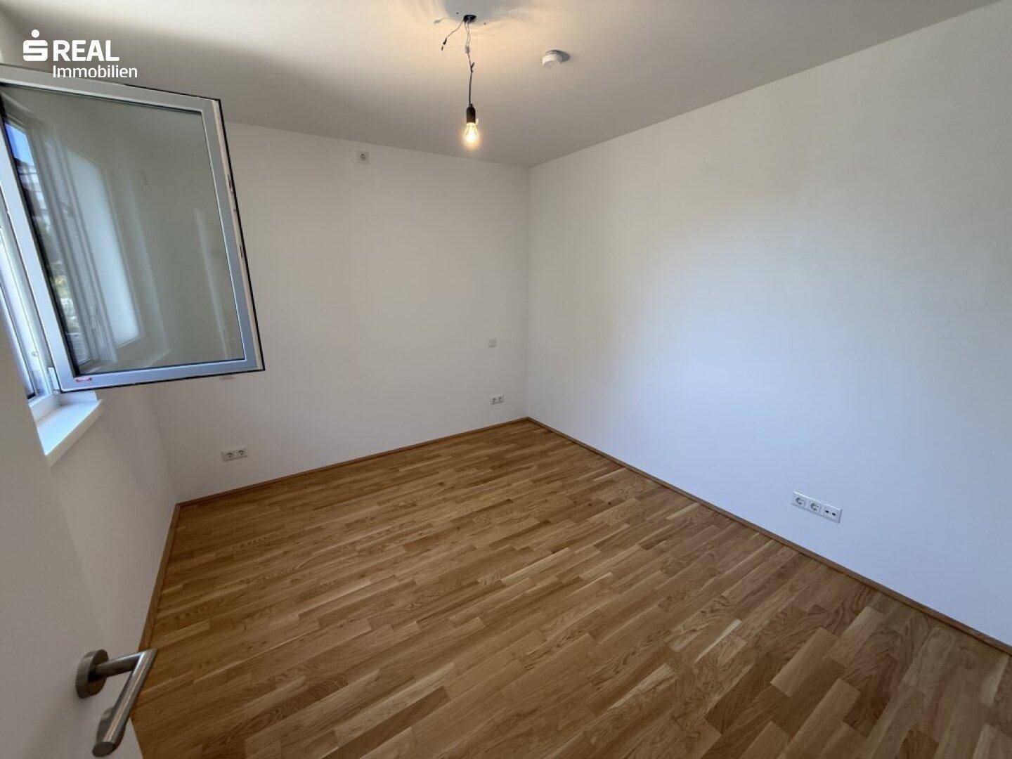 Helles, unmöbliertes Zimmer mit Holzboden und einem großen Fenster, ideal als Schlaf- oder Arbeitszimmer.